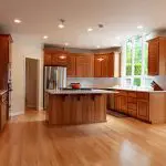 Kitchen cabinet refinishing process shown in a bright kitchen with natural wood cabinets, island, and updated finishes.