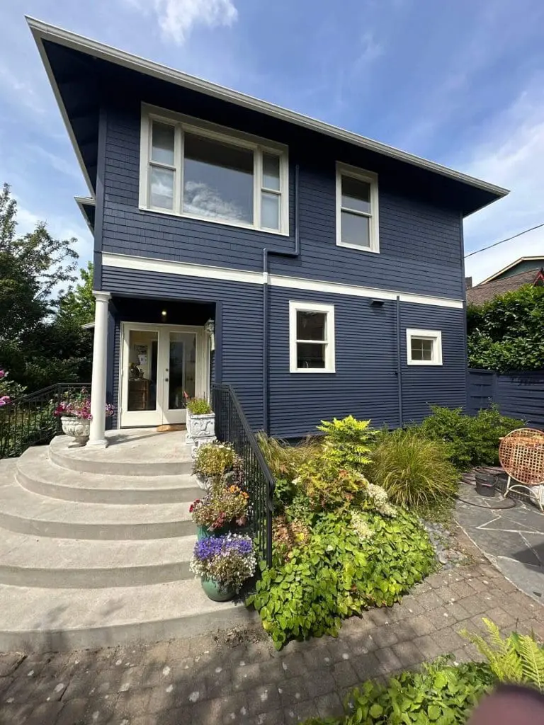 Navy blue horizontal lap siding garage with cream trim and garden greenery, professionally coated by Painters in Refined Painting LLC in Seattle, WA.