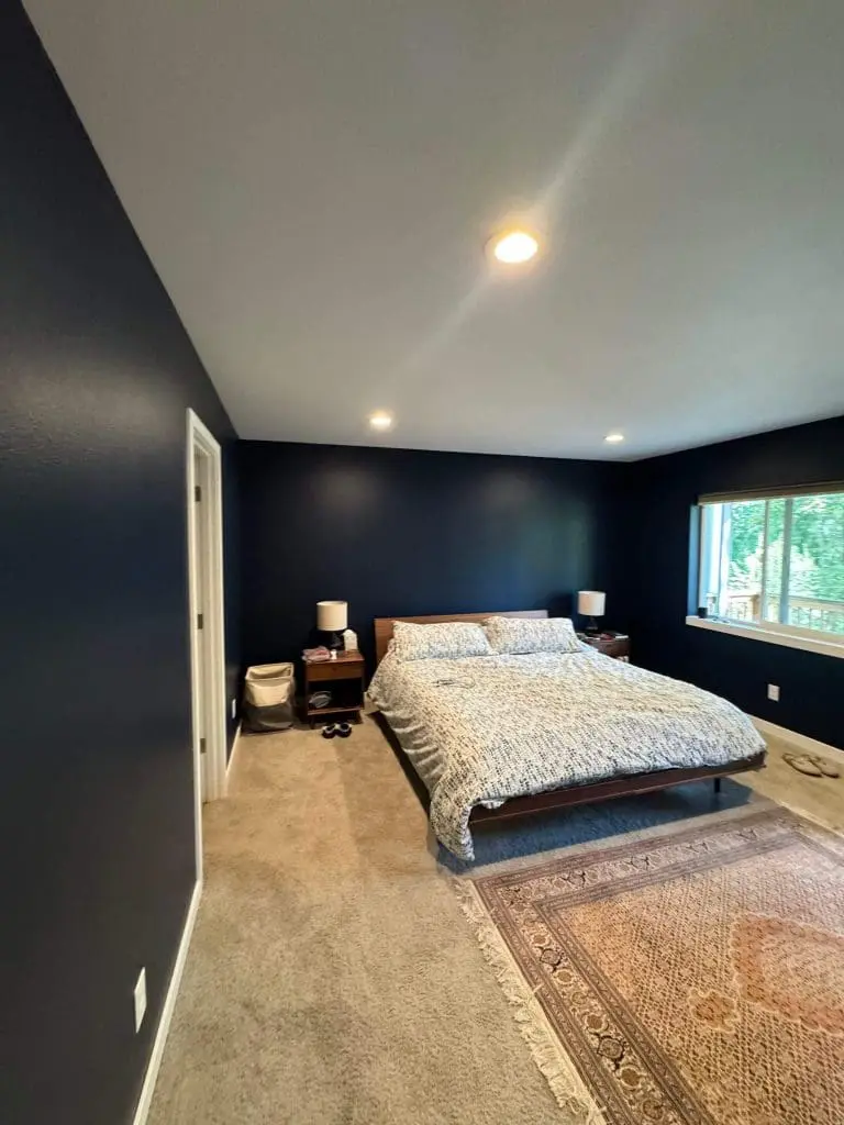A master bedroom with deep navy blue walls and wood furniture, showcasing the high-quality interior work of painters in Refined Painting LLC in Seattle, WA.