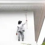 A painter using an extension roller to repaint the exterior of a Seattle home, illustrating how often you should repaint your home exterior.