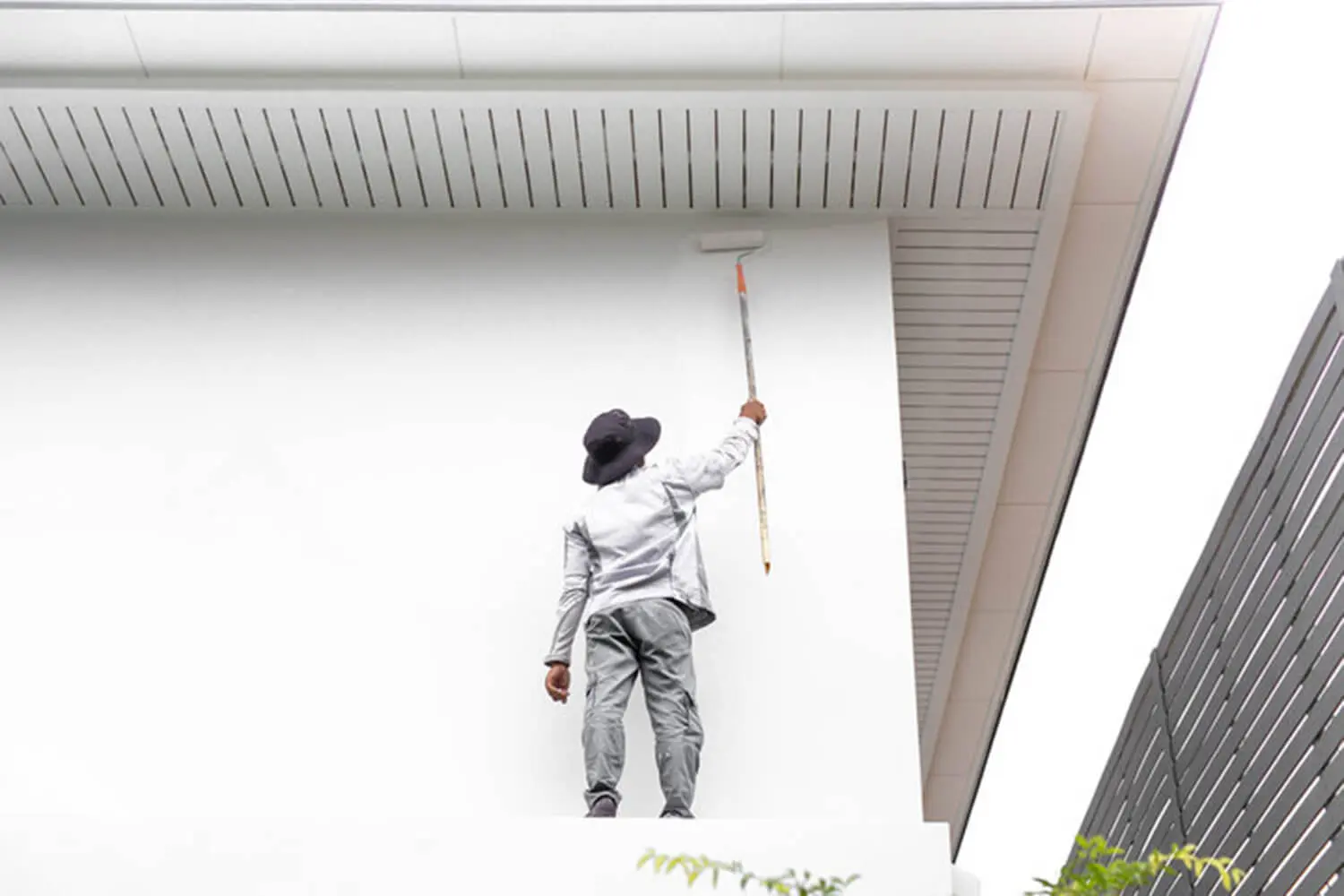A painter using an extension roller to repaint the exterior of a Seattle home, illustrating how often you should repaint your home exterior.